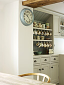 Uhr und Küchenkommode mit Tassen in einer Bauernhausküche in West Sussex, England, Vereinigtes Königreich