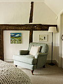 Light green upholstered armchair in corner of timber-framed bedroom of West Sussex farmhouse, England, UK