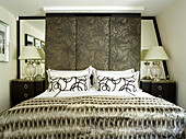 Glass lamps at bedside with large fabric covered headboard in London townhouse, UK