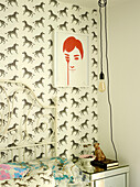 Framed print and lightbulb with zebra patterned wallpaper above bedside table London family home, UK