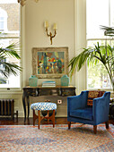 Blue velvet armchair and console in sash windows of London townhouse apartment, UK