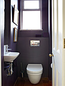 Small purple bathroom with uncurtained window in London townhouse apartment, UK