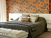 Grey blankets on double bed with orange floral wallpaper in London home, UK