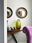 Convex mirrors above coloured glass vase on wooden side table in Manchester home, England, UK