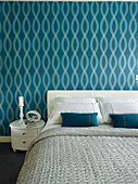 Blue patterned wallpaper above double bed with candle on side table in Manchester home, England, UK