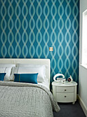 Blau gemusterte Tapete über dem Doppelbett mit weißem Beistelltisch in einer Wohnung in Manchester, England, UK