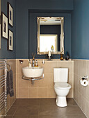 Silver-framed mirror above shelf in blue bathroom with tiling in Manchester home, England, UK