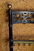 Carved black chair back and brown patterned wallpaper