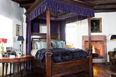 Antique four poster bed in bedroom of Scottish home with lit fire UK