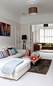 Light blue blanket on white sofa with coffee table set on rug in double room of contemporary London home, UK