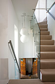 Glass staircase partition allowing natural light into narrow hallway of London home, England, UK