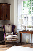 Purple upholstered chair below corner cabinet in historic country house