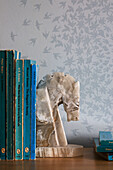 Books stacked on side unit with swallows wallpaper in London bedroom UK