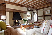 Lit fire in hearth of living room with beamed ceiling in East Sussex home, England, UK