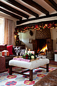 Fairylights garland above lit fire in timber framed Sussex home with tray of drinks on ottoman UK