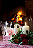 Wineglasses and lit candle with cut roses at fireside in Sussex home UK