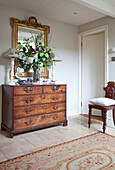 Flower arrangement with gilt mirror above wooden chest of drawers in Sussex home UK