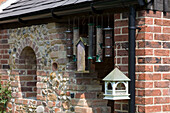 Bird feeders and birdhouse hang below guttering on stone and brick exterior of Suffolk home UK