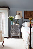 Tulips on table at side of brass bed in light blue Sussex farmhouse bedroom, UK