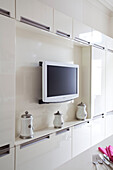 Wall mounted plasma screen TV in white kitchen of contemporary London home, UK