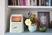 Nautical clock and cut wildflowers with book storage in Rye home, East Sussex, England, UK