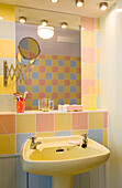 Multicoloured pastel tiles with yellow wash basin and shaving mirror in Rye home, East Sussex, England, UK