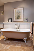 Freistehende Badewanne mit Rolltop und Kunstwerk im Badezimmer eines Hauses in Surrey, England, UK