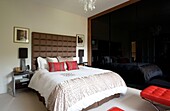 Double bed with upholstered headboard and black screened wardrobe in London home UK
