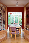 View through pale wood double doors to dining table with bookshelving in London home, England, UK