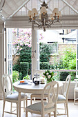 Weiß gestrichener Tisch für vier Personen im Wintergarten eines modernen Londoner Stadthauses mit Blick durch ein Fenster auf den Garten, England, UK
