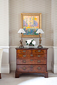 Matching lamps and artwork with antique wooden chest of drawers in contemporary London home, England, UK