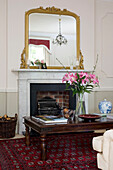 Cut lilies on wooden coffee table in front of fireplace with gilt mirror in classic Tyne & Wear home, England, UK