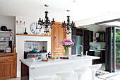 Matching chandeliers above breakfast bar in contemporary kitchen with clock above range oven in London home, UK