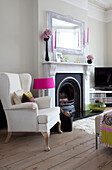 White armchair at fireplace with contemporary mirror in London home, UK
