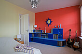 Hellblaues Regal und E-Gitarren vor roter Wand im Schlafzimmer eines Hauses im Retrostil in East Sussex, England, UK