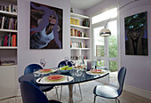 Blauer Esstisch mit moderner Kunst und Bücherregalen in einem Retro-Haus in East Sussex, England, UK