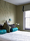 Oriental style wall decor and upholstered cushions in bedroom of contemporary London townhouse, England, UK