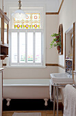 Sonnendurchflutetes Badezimmer mit originalen Buntglasfenstern, Waschtisch und freistehender Badewanne in einem Stadthaus in London, England, Vereinigtes Königreich