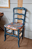 Blau gestrichener Stuhl mit Blumenkissen in einem Bauernhaus in Kent (England)