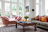 PInk double arm chaise with carved wooden coffee table in living room of contemporary London family home, UK