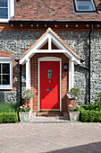 Red front door of stone Kent cottage with drainpipes in Kent, England, UK