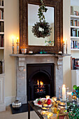 Carved wooden mirror frame above lit fire in London living room, UK