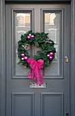 Floral wreath with pink ribbon and baubles on grey front door of London townhouse, UK