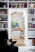 Schwarzer Sessel im Arbeitszimmer mit Bücherregalen und Blick in eine moderne Küche in einem Londoner Haus, UK