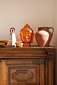 Pottery jug and Buddha's head on carved wooden cabinet in London home, UK