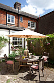 Gartentisch und Stühle im Schatten eines Sonnenschirms im Garten eines Landhauses in Sussex, England, UK