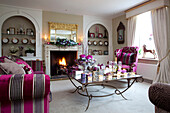 Vibrant pink upholstered sofa and chair in living room of Surrey farmhouse with lit tealights on coffee table, England, UK