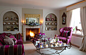 Rosa gestreiftes Sofa und Sessel im Wohnzimmer eines Bauernhauses in Surrey mit Teelichtern auf dem Couchtisch, England, UK