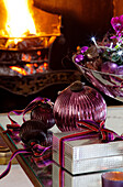 Vintage purple baubles and gift wrapped present on table in Surrey farmhouse with lit fire, England, UK
