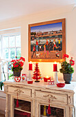 Lit candles with geraniums on painted sideboard in Surrey farmhouse, England, UK